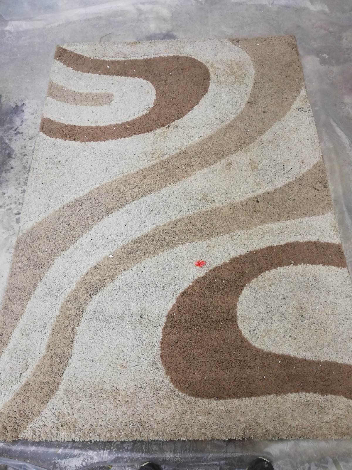 Alfombra decorativa café con diseño ondulado, con manchas y polvo acumulado