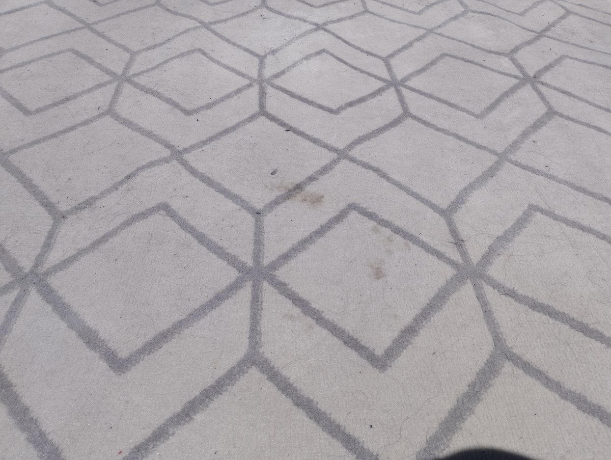 Alfombra de rombos gris claro con una mancha visible